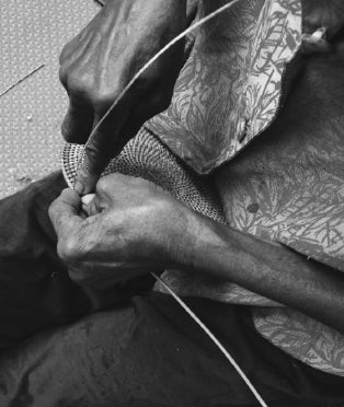 Black and white image of person's hand weaving straw