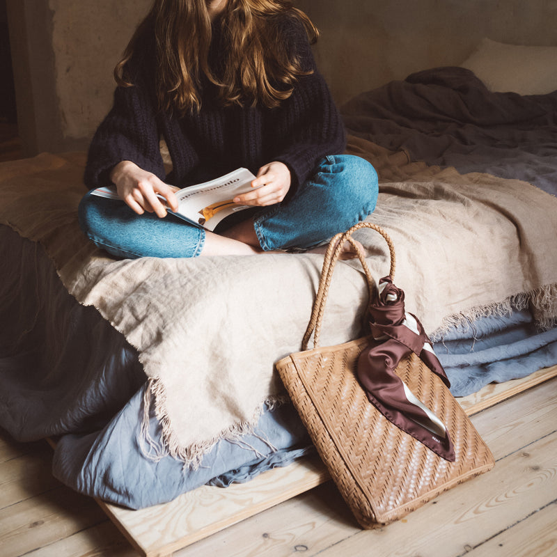 Bembien Le Tote in Caramel on the floor alongside a woman seated on a bed reading a book