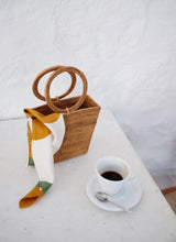 Bembien Soleil Scarf placed on the Chloe Bag in Rattan on top of a table and alongside a cup of coffee