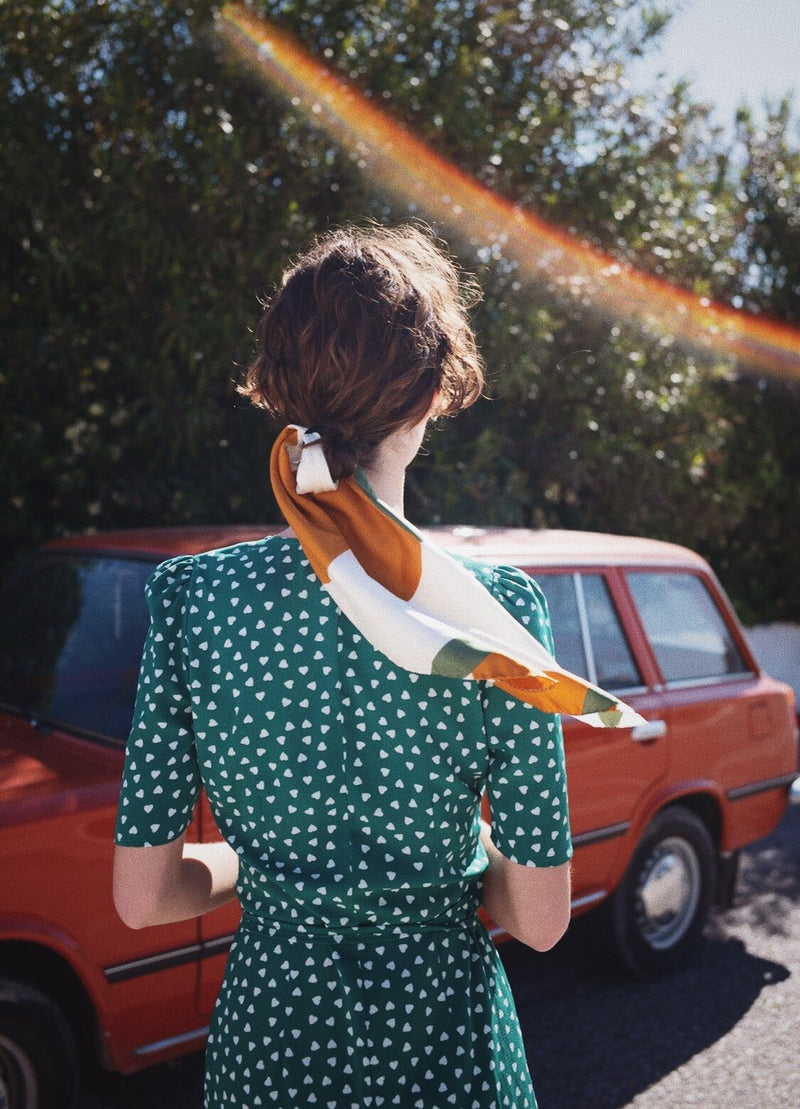 Bembien Soleil Scarf in Clementine worn by a woman in her hair standing outside next to a car