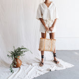 Bembien Margot Bag in Medium Caramel Rattan in the hands of a standing woman next to a plant